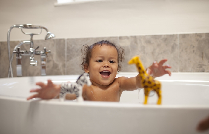 Lachende peuter speelt in bad met speelgoedgiraf en -zebra op de badrand, badtijd peuter