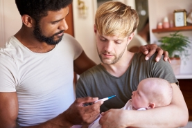 Homokoppel met baby in de armen, twee vaders nemen de temperatuur van hun zieke baby met thermometer