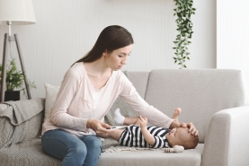 Mama met baby in de zetel, moeder neemt de temperatuur van haar zieke baby met thermometer