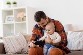 papa kijkt met baby op schoot naar smartphone in de zetel