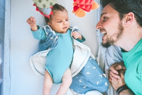 papa lacht naar baby in bed, baby draagt slaapzak
