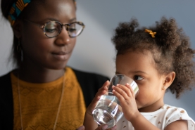 Kind drinkt water uit glas terwijl mama ernaar kijkt