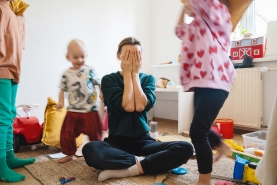 opvoedstress_mama zit op de grond met handen voor haar gezicht, terwijl haar kinderen rond haar lopen