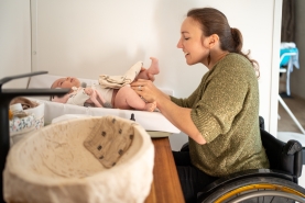 Vrouw in rolstoel ververst de luier van haar kind