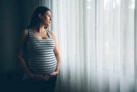 zwanger vrouw kijkt peinzend door het venster
