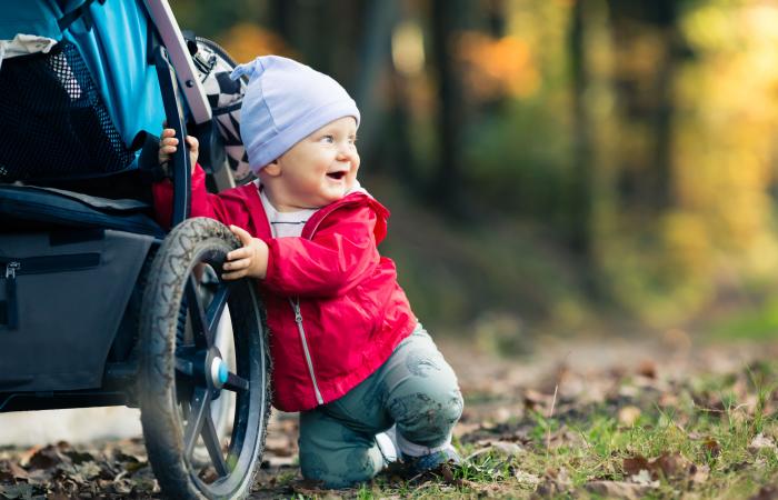 Peuter houdt zich in het bos staande tegen een kinderwagen