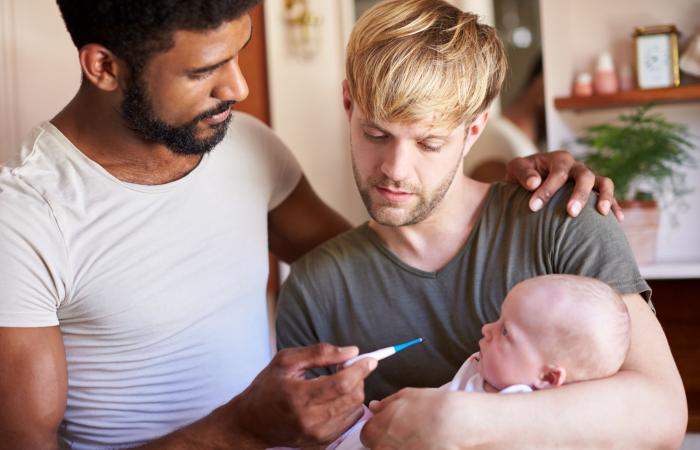 Homokoppel met baby in de armen, twee vaders nemen de temperatuur van hun zieke baby met thermometer