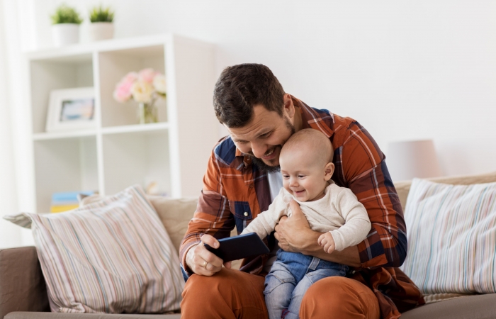 papa kijkt met baby op schoot naar smartphone in de zetel