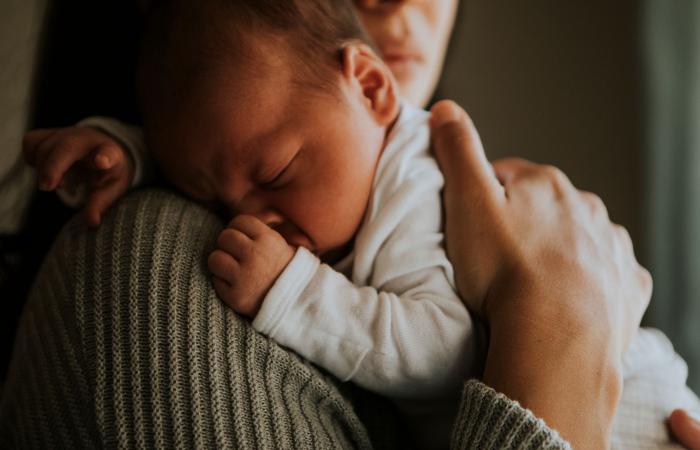 Baby slaapt op schouder van ouder met duim in mond