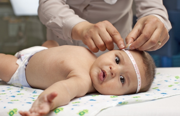 baby ligt op matje terwijl vrijwilliger de hoofdomtrek meet in consultatiebureau