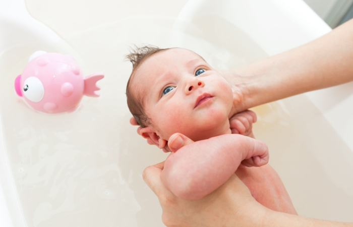 Ouder geeft baby een bad, baby in bad met een roze goudvis