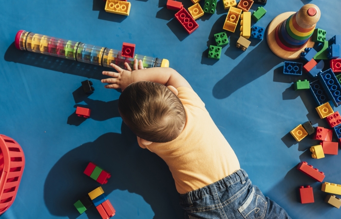 Kind speelt op zijn buik met felgekleurde blokken en ringen in de kinderopvang