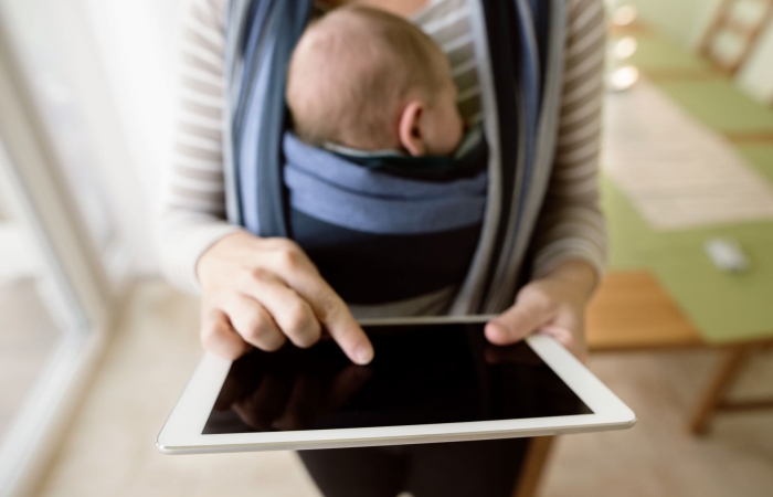 Mama draagt kindje in draagzak en gebruikt haar tablet