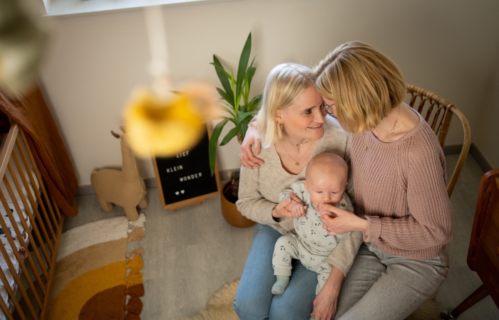 Koppel knuffelt met baby op de schoot in kinderkamer, mama's met kind, kader met tekst lief klein wonder