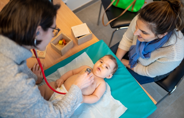 Arts in een consultatiebureau onderzoekt baby met stethoscoop en ouder kijkt