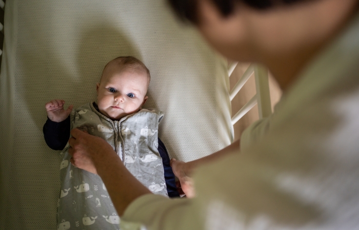 Mama legt baby te slapen in babybed, slaapritueel in veilige slaapomgeving