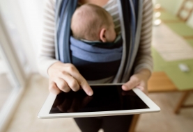 Mama draagt kindje in draagzak en gebruikt haar tablet