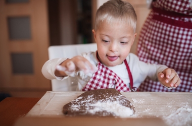 Jongen met downsyndroom maakt deeg klaar met ouder in de keuken
