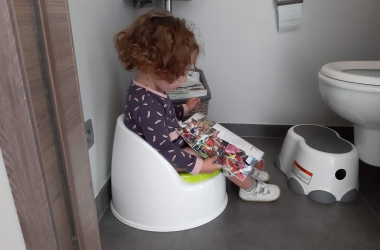 Meisje zit op het potje en leest een boekje