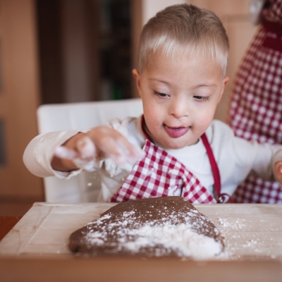 Jongen met downsyndroom maakt deeg klaar met ouder in de keuken