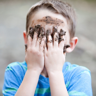 Jongen met modder aan handen bedekt zijn gezicht