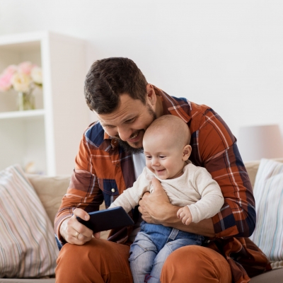 papa kijkt met baby op schoot naar smartphone in de zetel