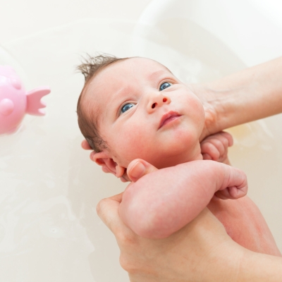 Ouder geeft baby een bad, baby in bad met een roze goudvis