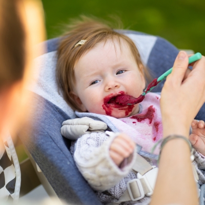 Roodharige baby eet groentepap van biet met lepel in wippertje