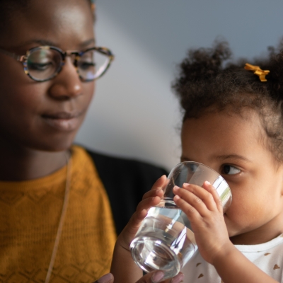 Kind drinkt water uit glas terwijl mama ernaar kijkt