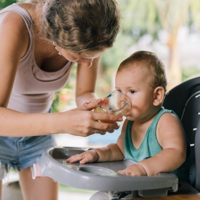 Mama geeft een baby te drinken in stoeltje