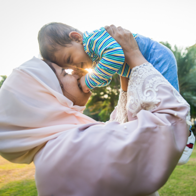 Vrouw met hoofddoek tilt haar kind op en kijken al lachend in elkaars ogen