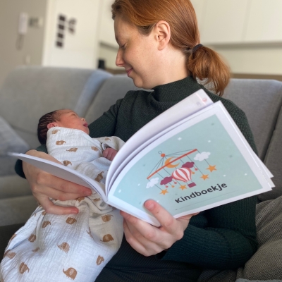 Mama leest Kindboekje met kindje op de arm in de zetel