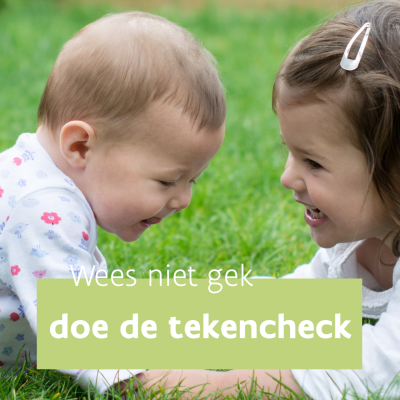 twee lachende kindjes liggen in buiklig op het gras