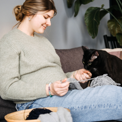 Zwangere vrouw zit in zetel met haar kat, breien op de sofa.