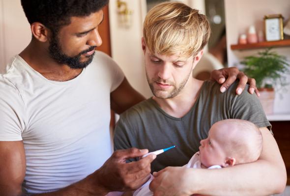 Homokoppel met baby in de armen, twee vaders nemen de temperatuur van hun zieke baby met thermometer