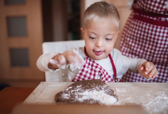 Jongen met downsyndroom maakt deeg klaar met ouder in de keuken