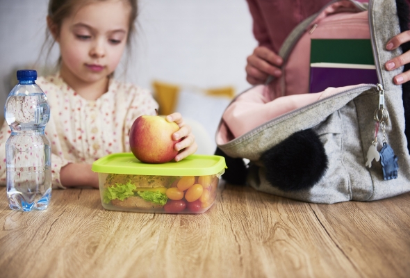 Meisje vult schooltas met brooddoos, appel en flesje water