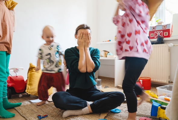 opvoedstress_mama zit op de grond met handen voor haar gezicht, terwijl haar kinderen rond haar lopen