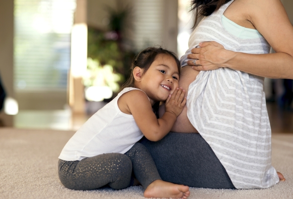 Peuter legt hoofd op buik van zwangere mama, gezinsuitbreiding met broer of zus