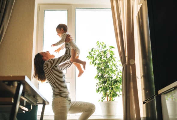 Mama tilt spelend haar baby op, lachende baby aan raam