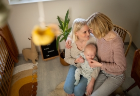 Koppel knuffelt met baby op de schoot in kinderkamer, mama's met kind, kader met tekst lief klein wonder
