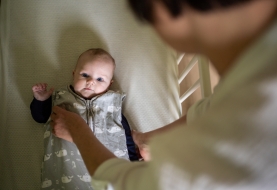 Mama legt baby te slapen in babybed, slaapritueel in veilige slaapomgeving