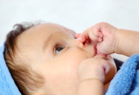 baby is op zijn duim aan het zuigen na badje ingerold in handdoek