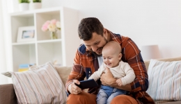 papa kijkt met baby op schoot naar smartphone in de zetel