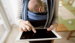 Mama draagt kindje in draagzak en gebruikt haar tablet
