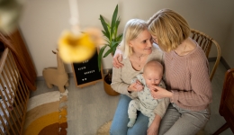 Koppel knuffelt met baby op de schoot in kinderkamer, mama's met kind, kader met tekst lief klein wonder